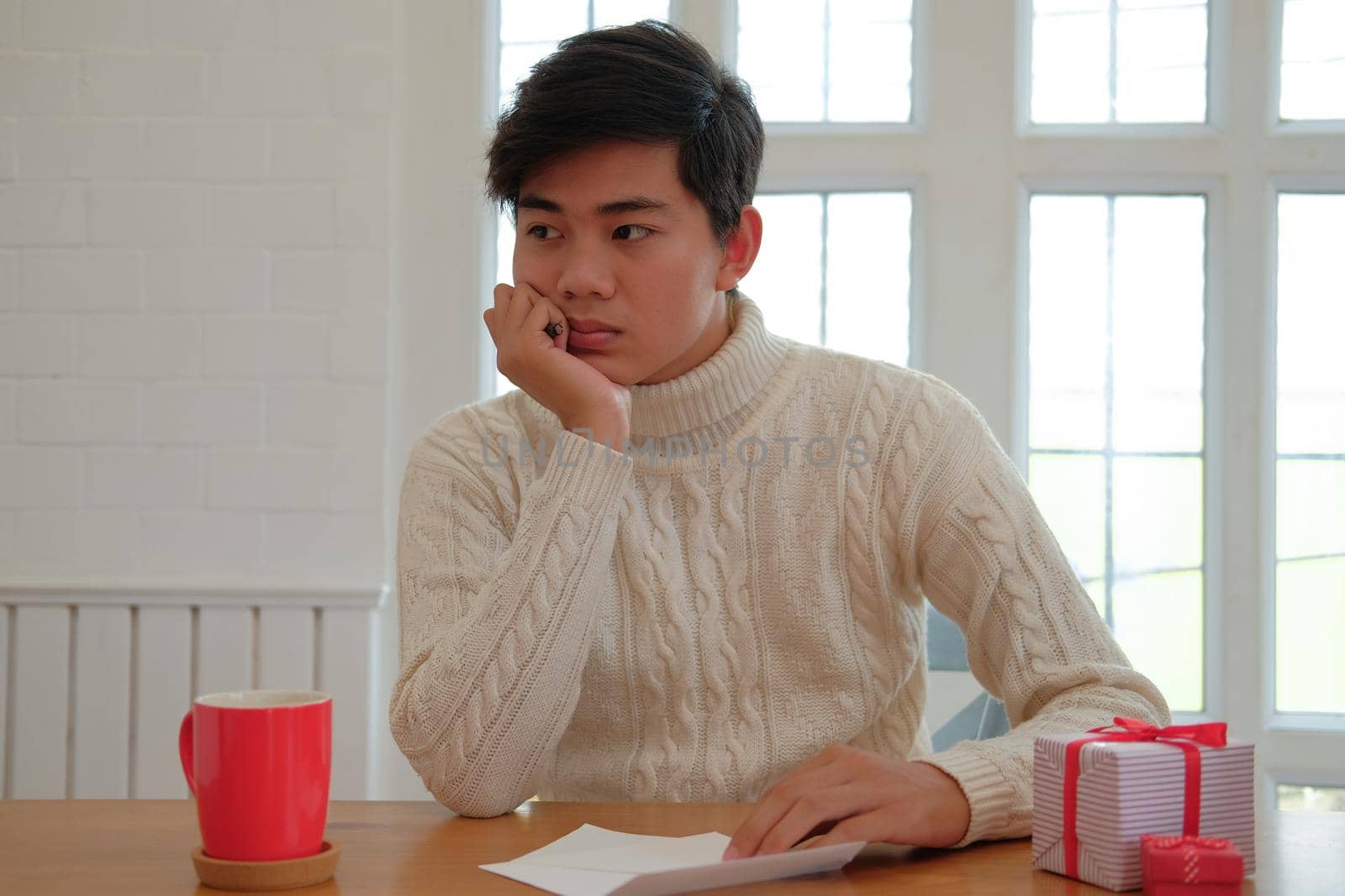 man wearing cream sweater thinking what to write on christmas letter greeting card holiday wishes. xmas celebration