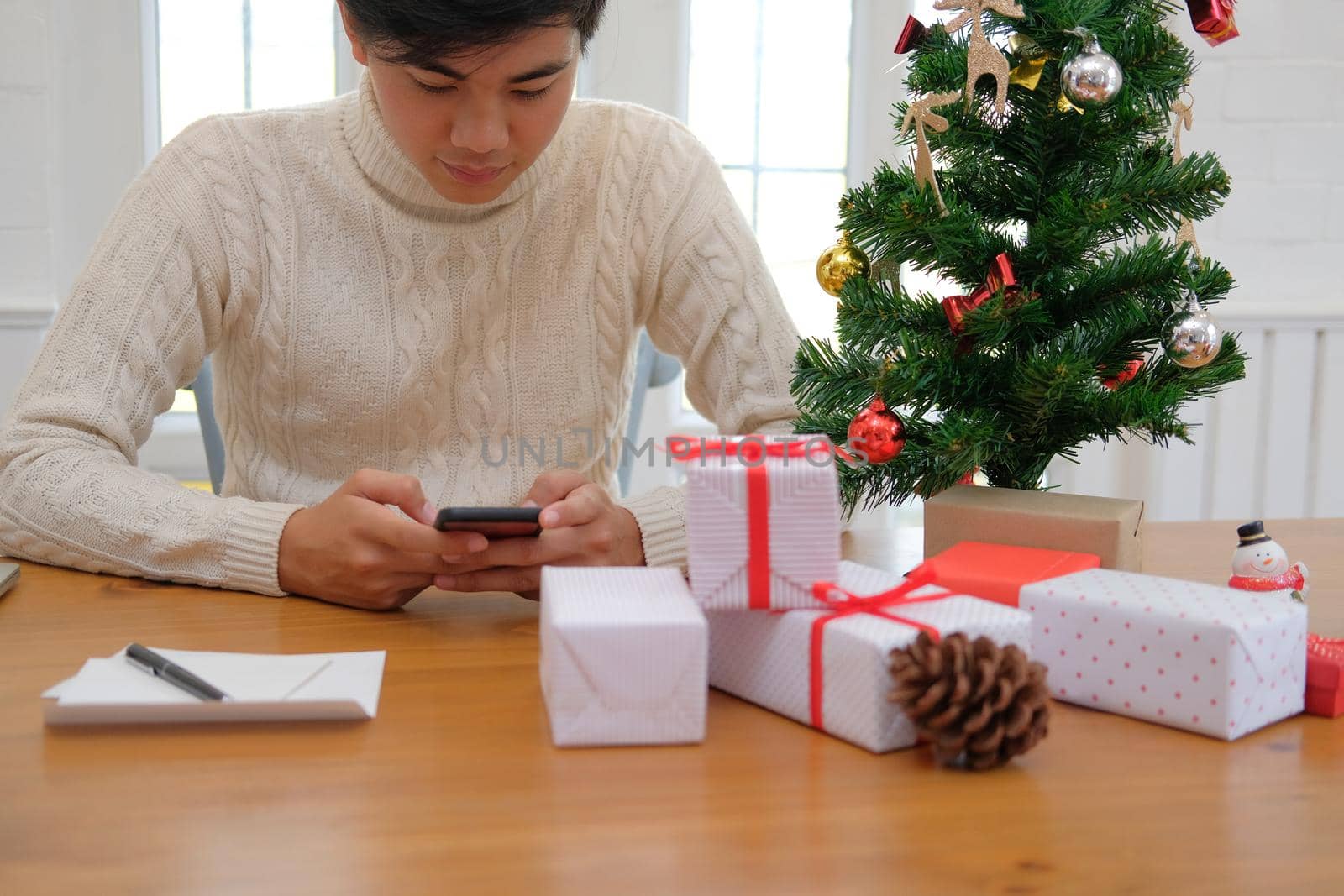 man wearing cream sweater using mobile smart phone with christmas decoration. xmas new year holiday celebration.