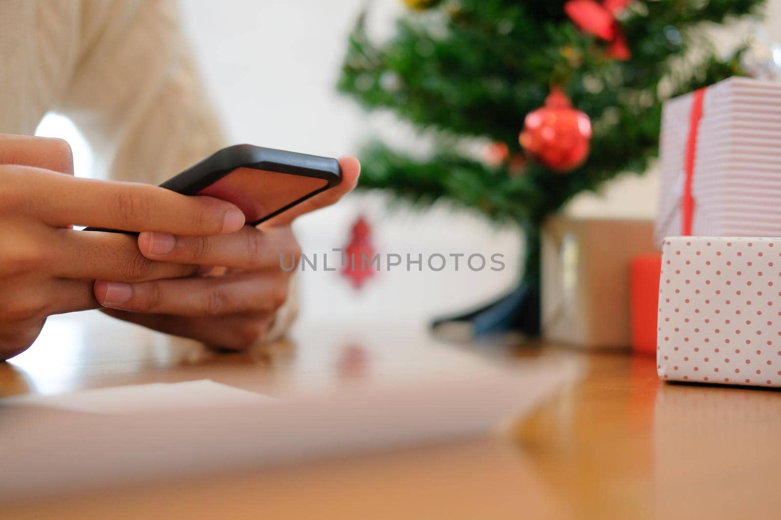 man wearing cream sweater using mobile smart phone with christmas decoration. xmas new year holiday celebration.