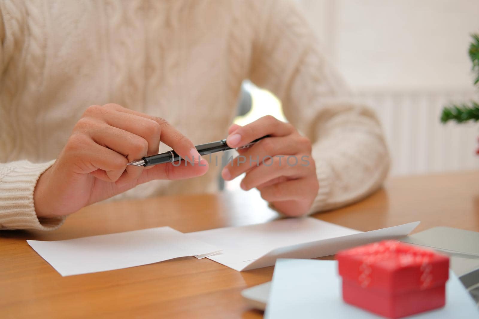 man wearing cream sweater thinking writing christmas letter greeting card holiday wishes with xmas decoration.