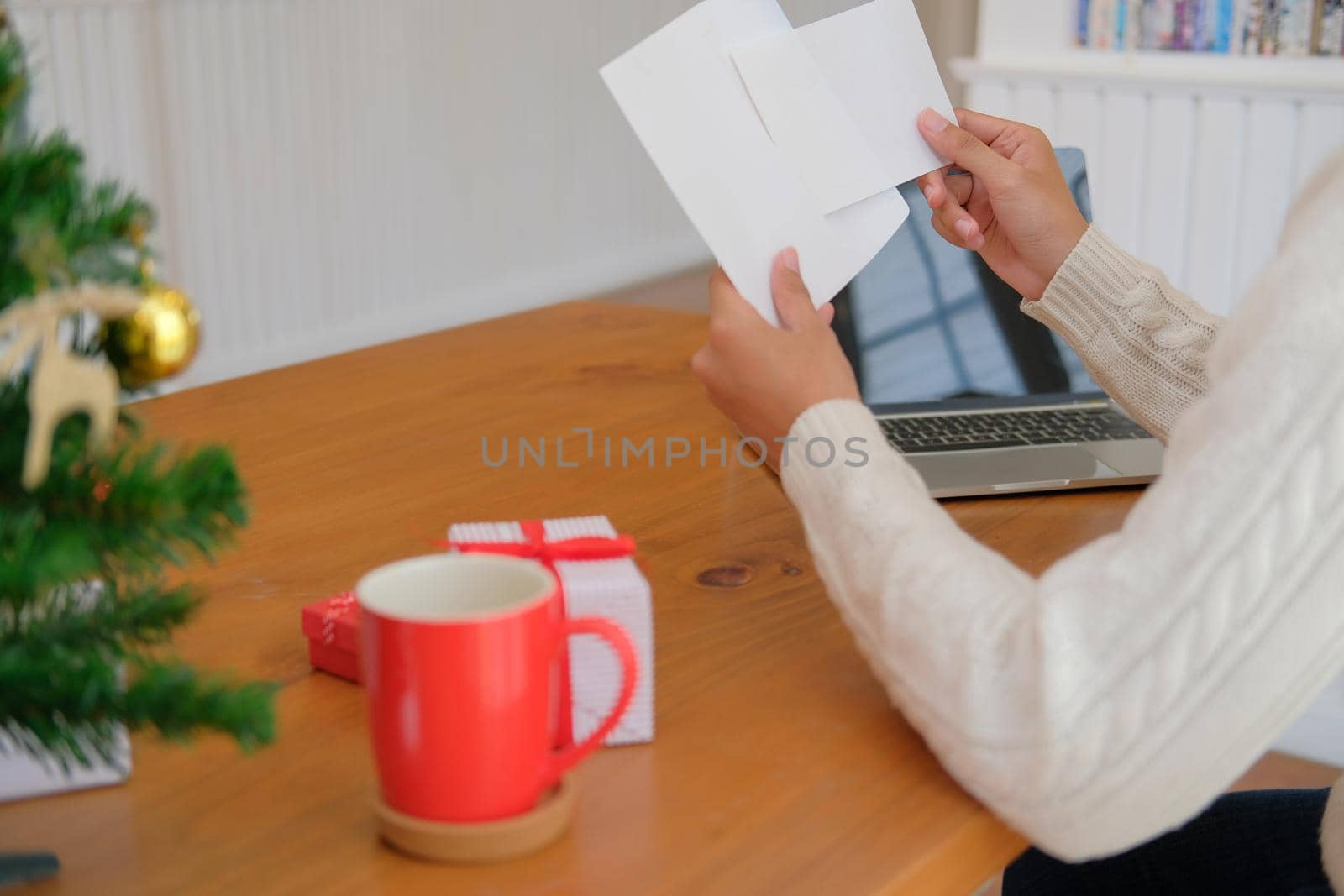 man wearing cream sweater opening sending christmas letter greeting card holiday wishes with xmas decoration
