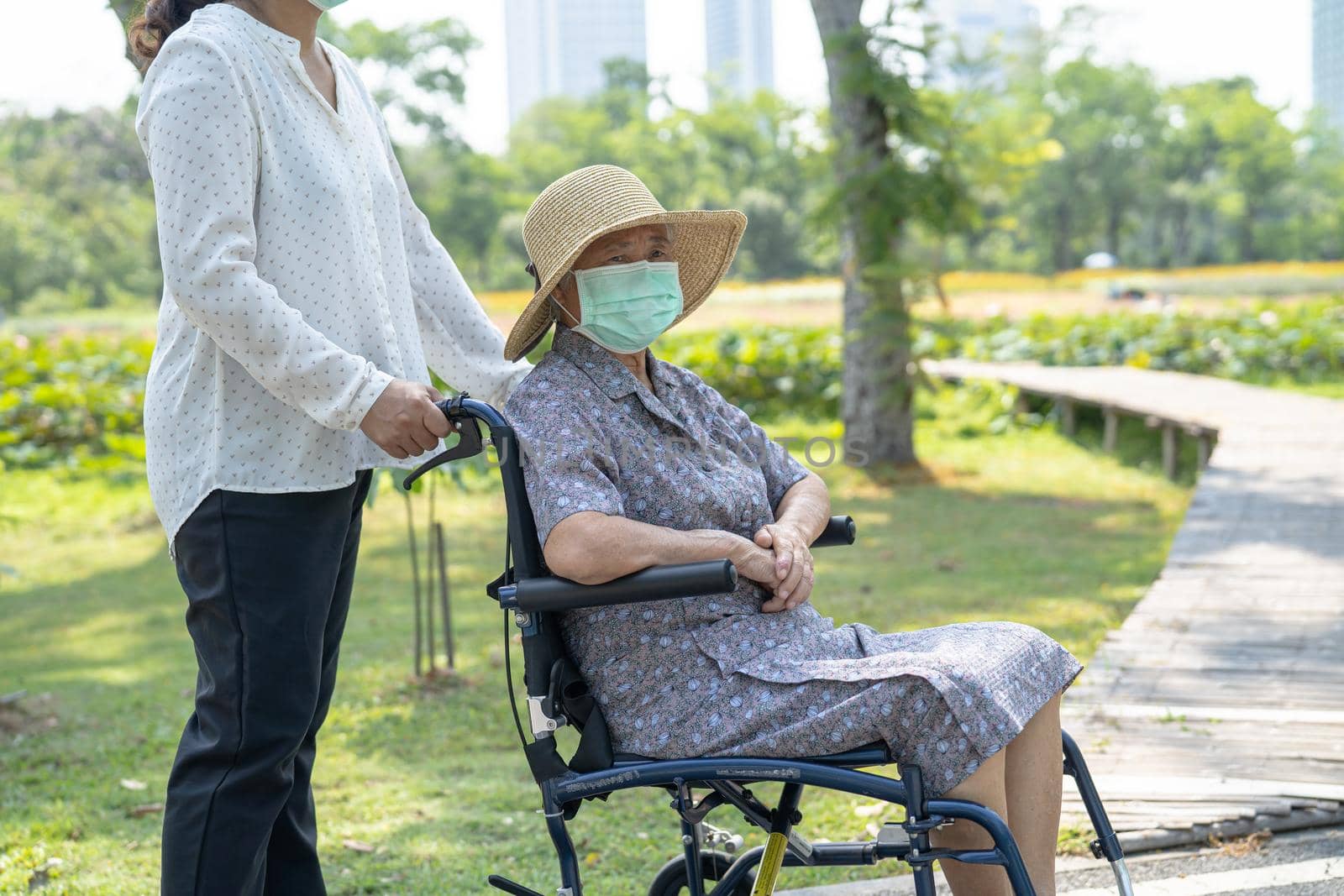 Help Asian senior or elderly old lady woman on wheelchair and wearing a face mask for protect safety infection Covid-19 Coronavirus in park.