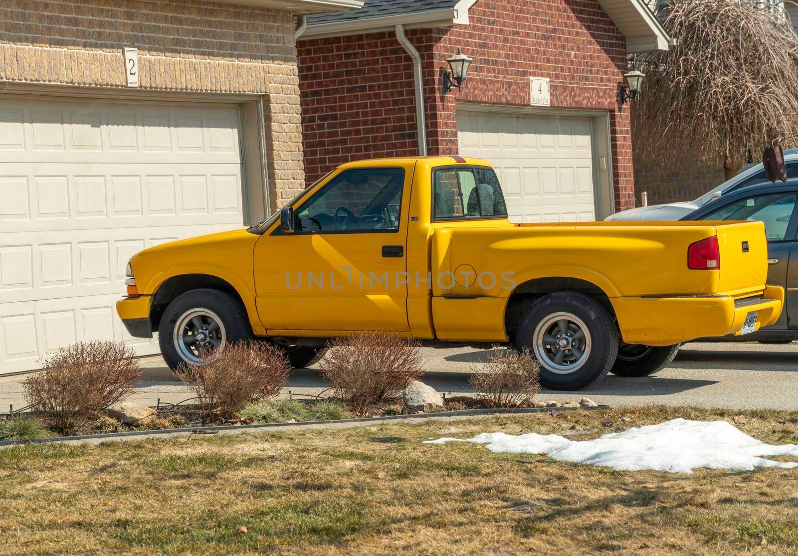 A beautiful yellow pickup truck stands near the garage on a warm day in early spring.
