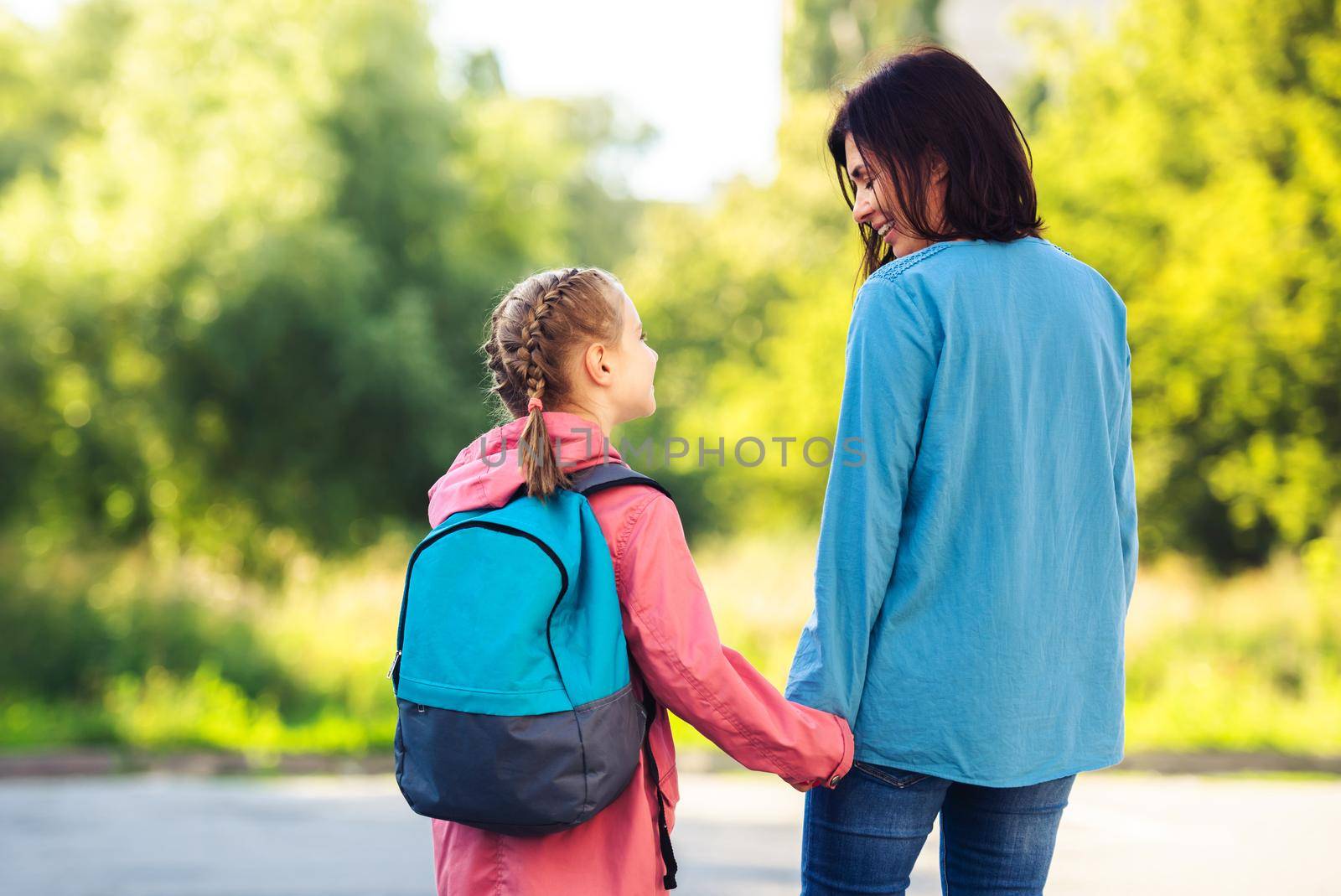 Rear view of mother and schoolgirl holding hands walking along car parking