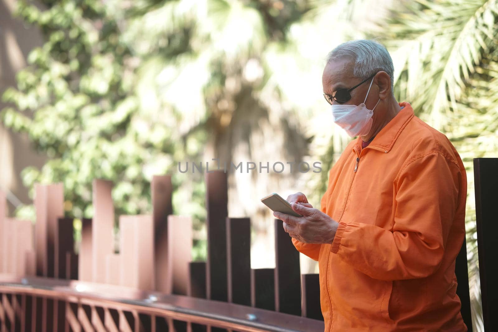 asian old elder senior man elderly wearing mask using mobile smart phone cellphone outdoor. mature retirement lifestyle