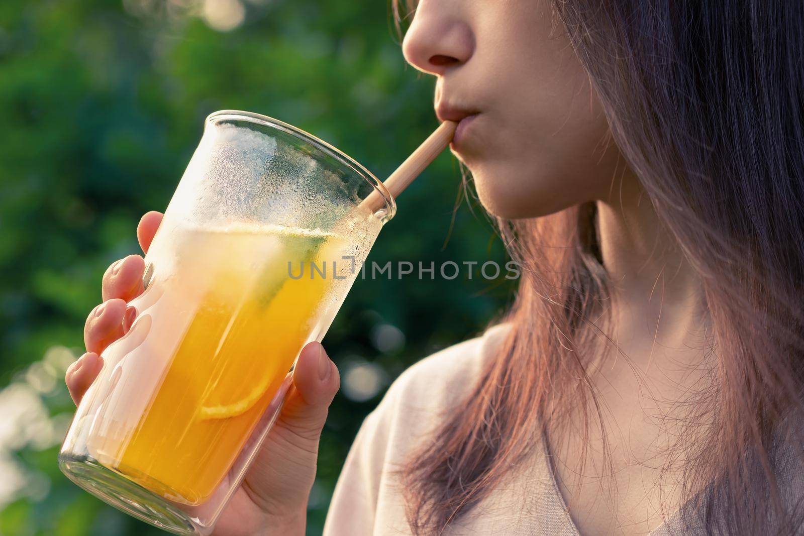 Girl drinks from a glass with fresh orange summer cocktail, close-up, selective focus.