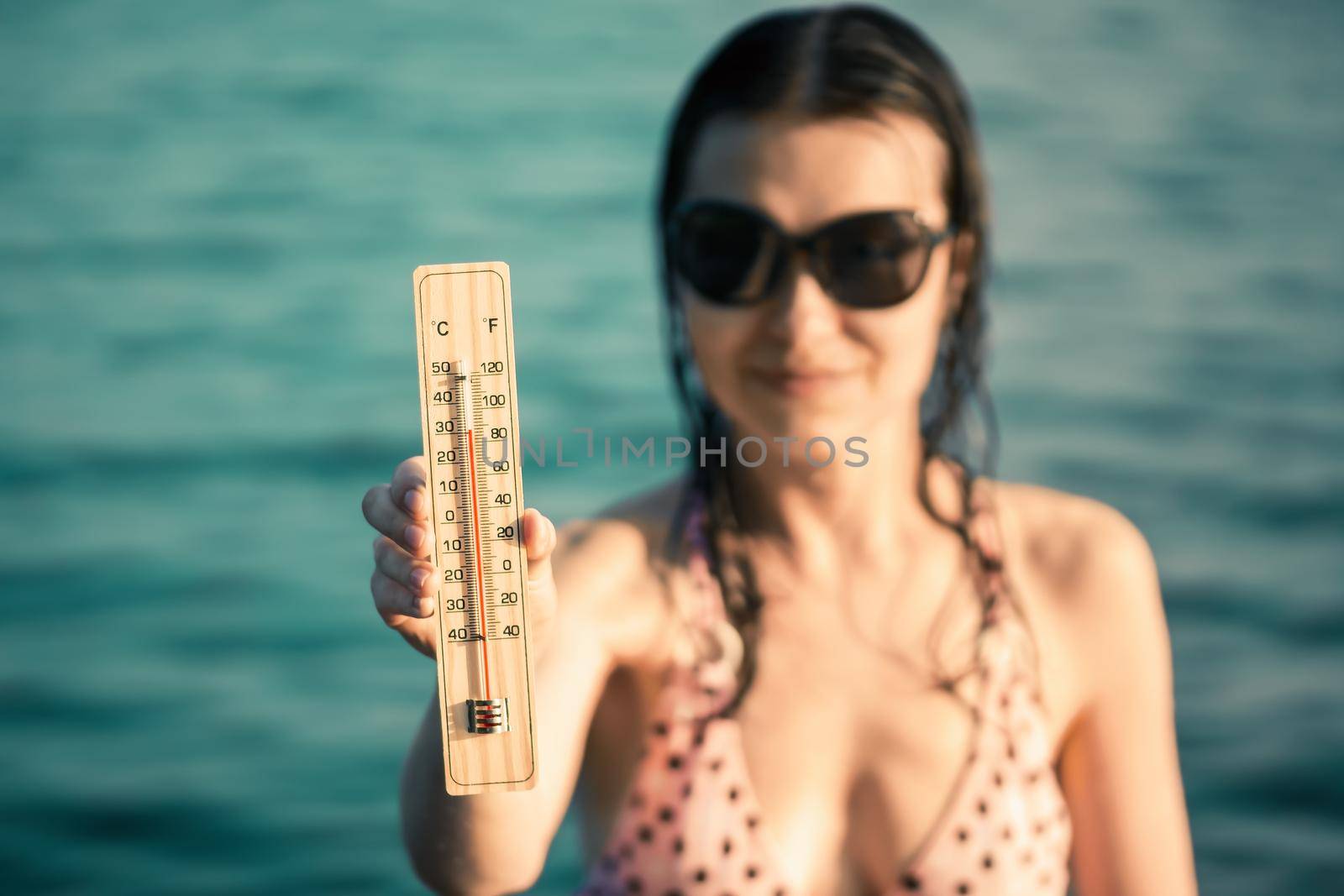 Beautiful young woman in sunglasses with a thermometer in her hand on the background of the sea. Summer vacation and heat concept, selective focus by galsand