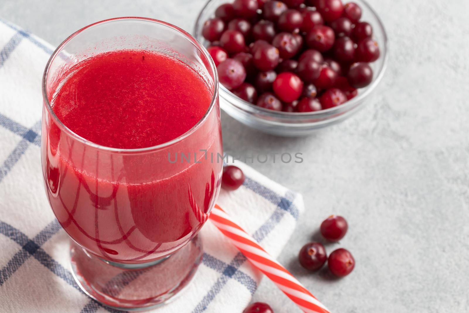 One glass with homemade freshly cranberry juice and a bowl of cranberries on a gray concrete table.