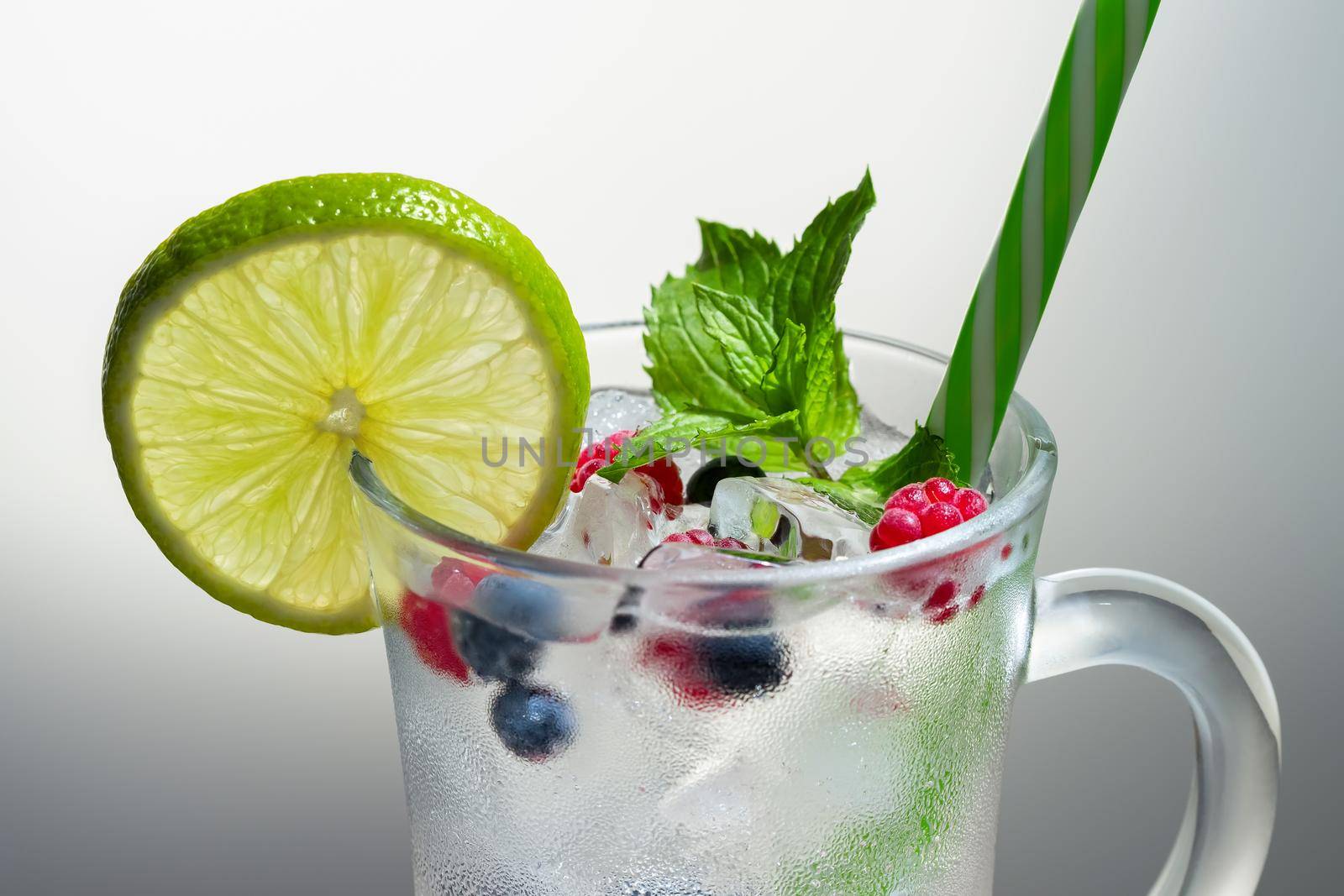 Refreshing summer cocktail with ice, lime and berries in a glass with a straw by galsand