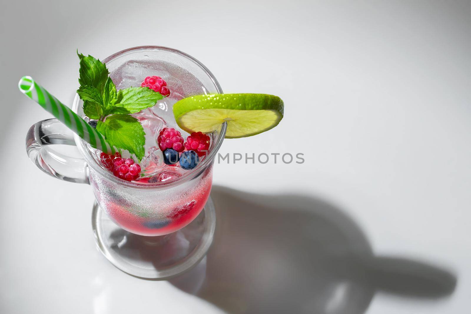 Refreshing summer cocktail with ice, lime and berries in a glass with a straw, copyspace by galsand