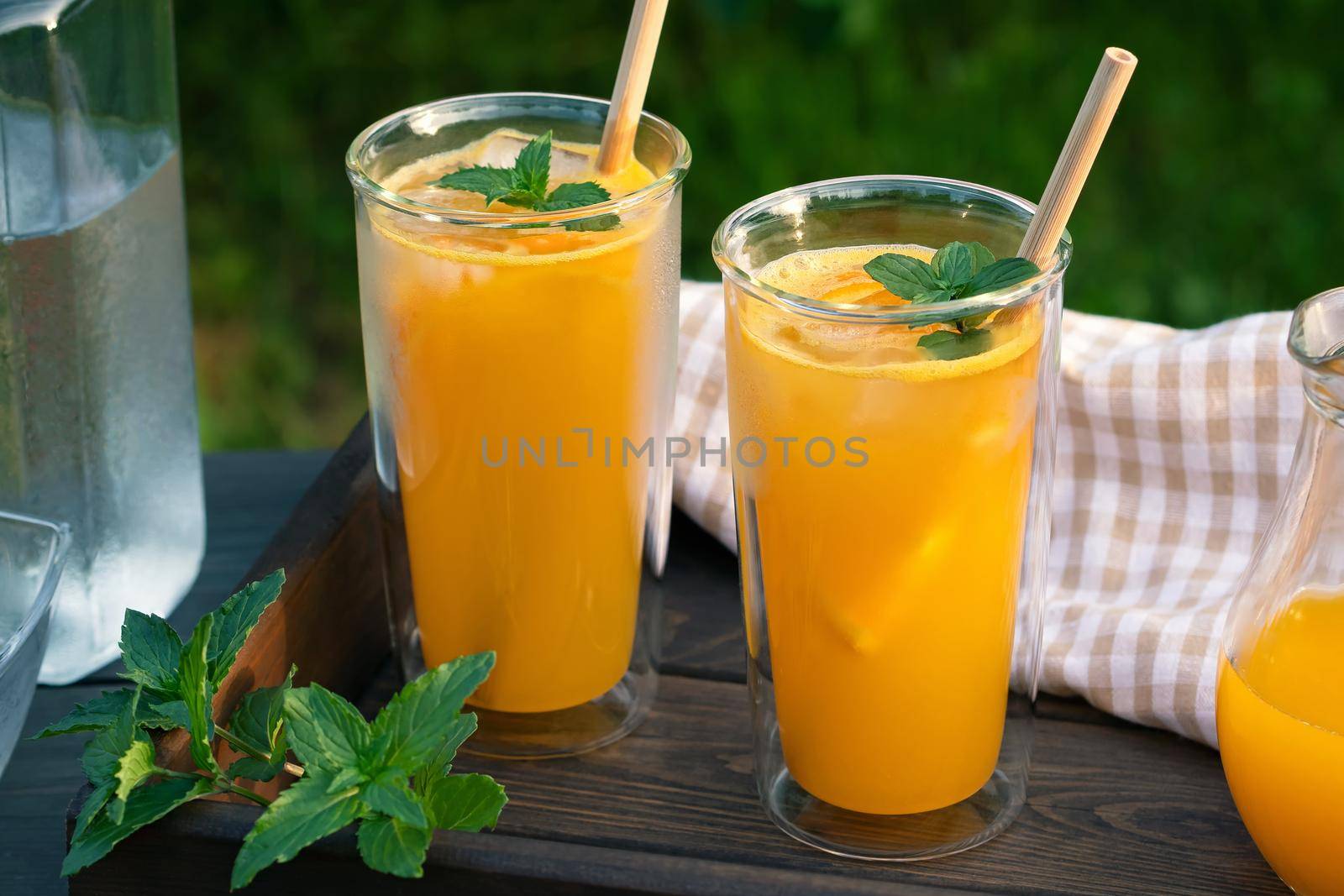 Refreshing summer homemade orange cocktail in tall double glass glasses with mint and ice, selective focus by galsand
