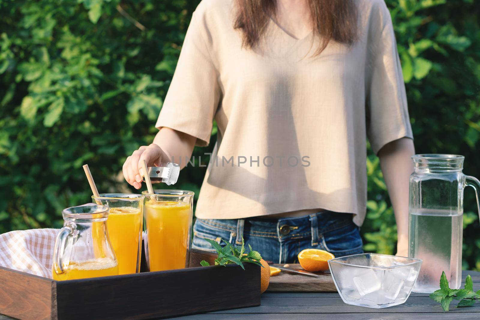 Girl cooking summer orange cocktail with mint and ice cubes outdoors, selective focus.