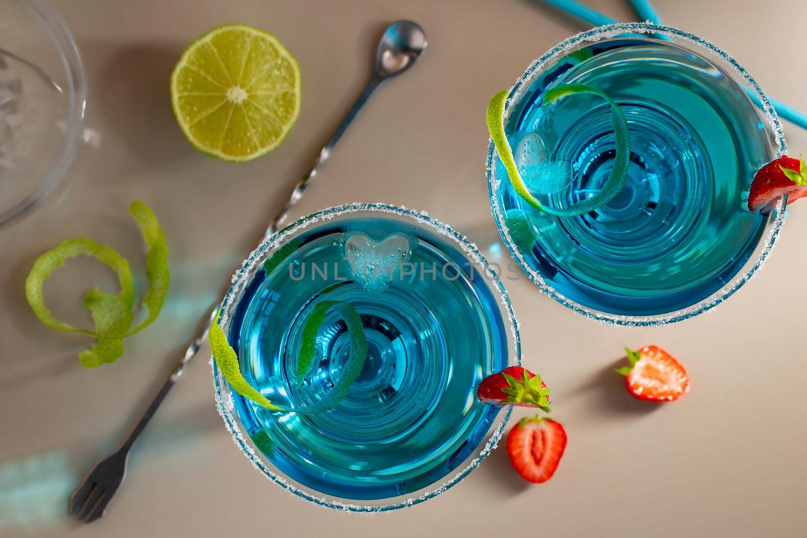 Fresh homemade blue margarita cocktail garnished with lime zest and strawberries.