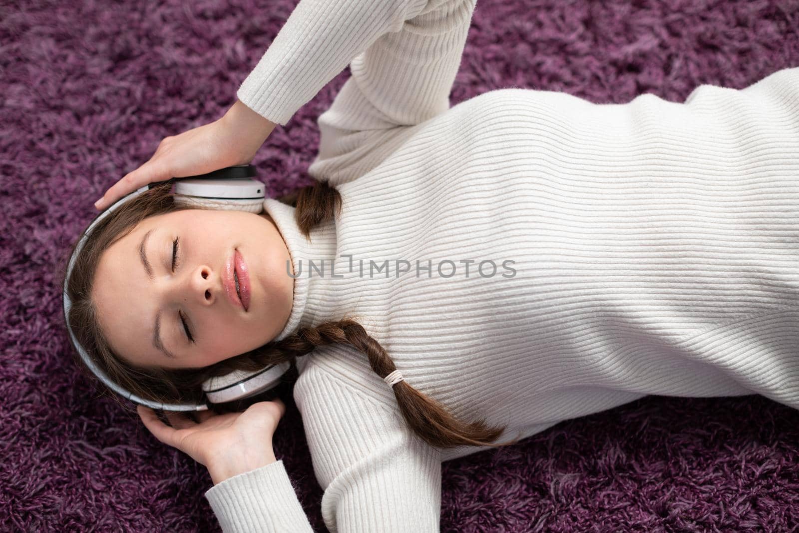 A brunette with pigtails and headphones on her ears lies on the carpet with her eyes closed and listens to her favorite music. A friendly teenager.