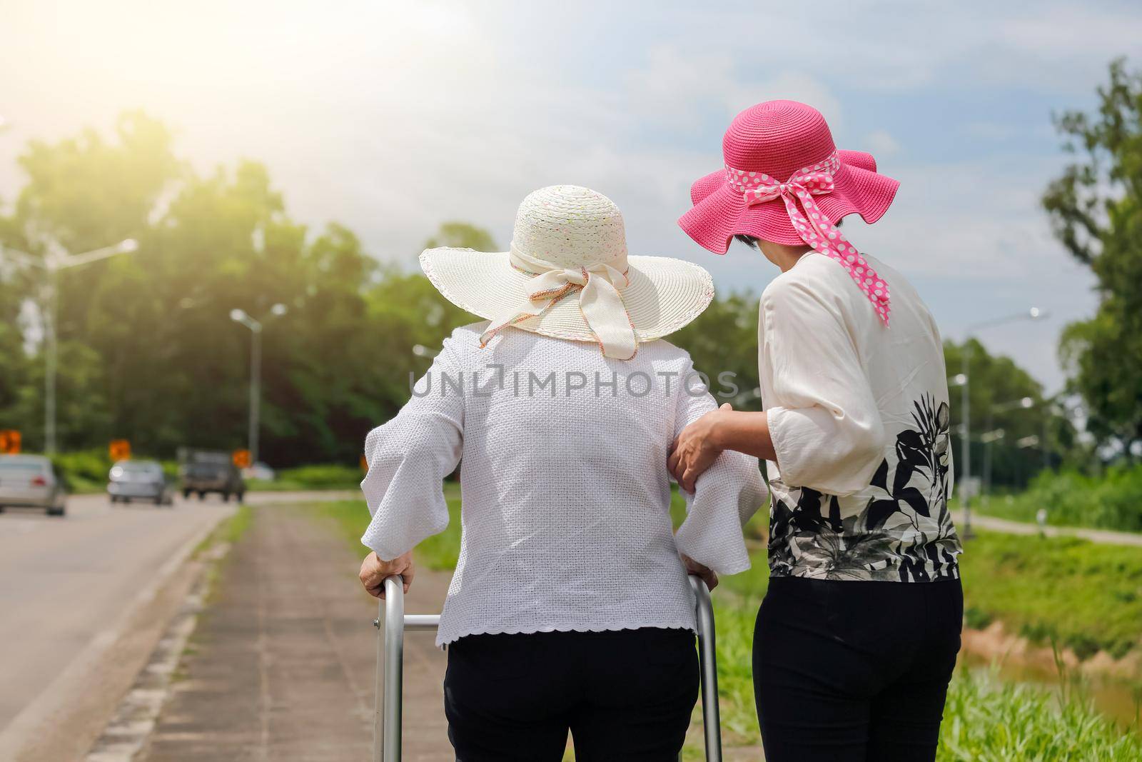 Daughter take care elderly woman walking on street in strong sunlight.