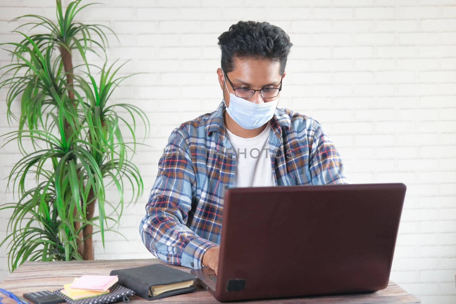 Businessman in face mask working on laptop .