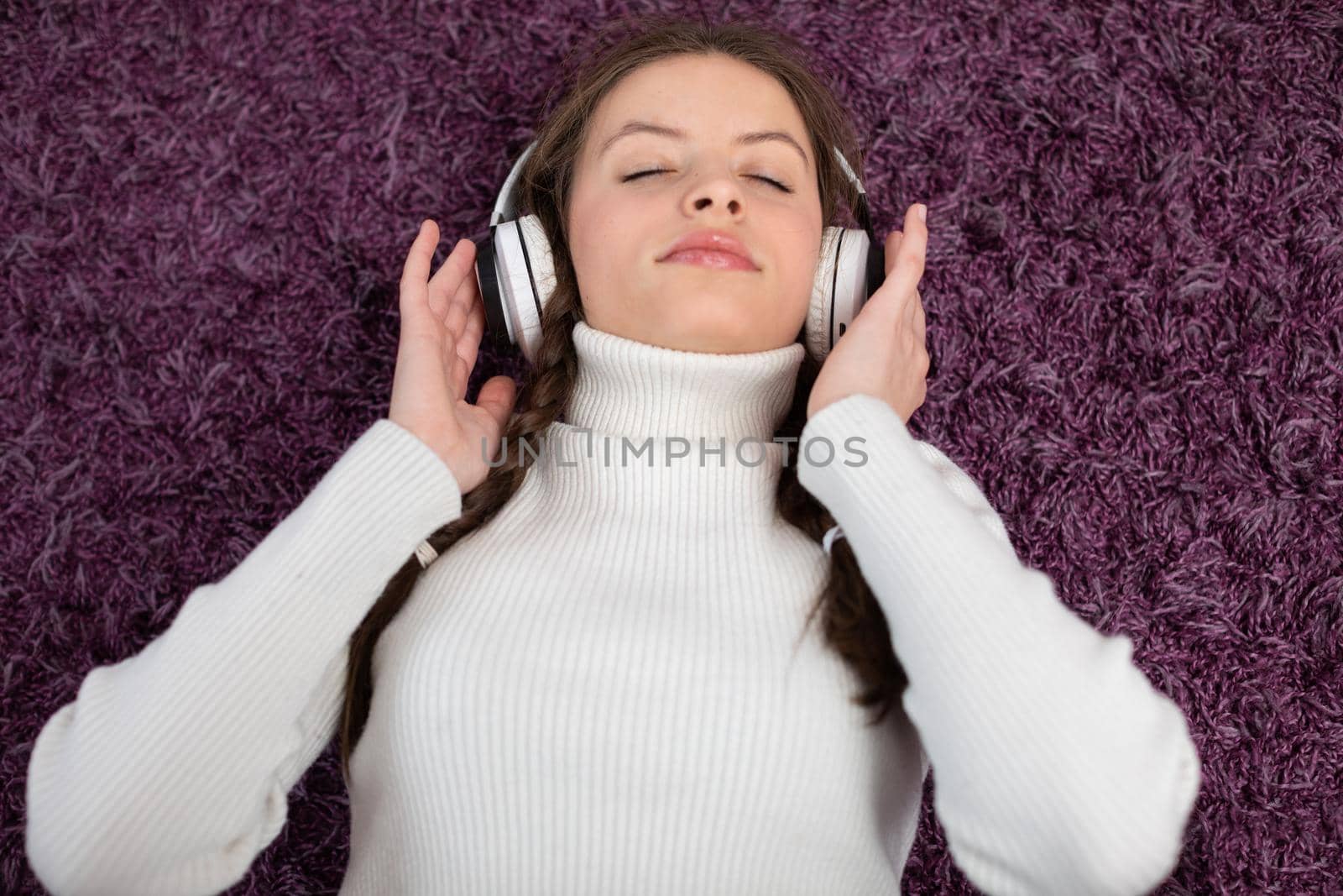 A brunette with pigtails and headphones on her ears lies on the carpet with her eyes closed and listens to her favorite music. A friendly teenager.