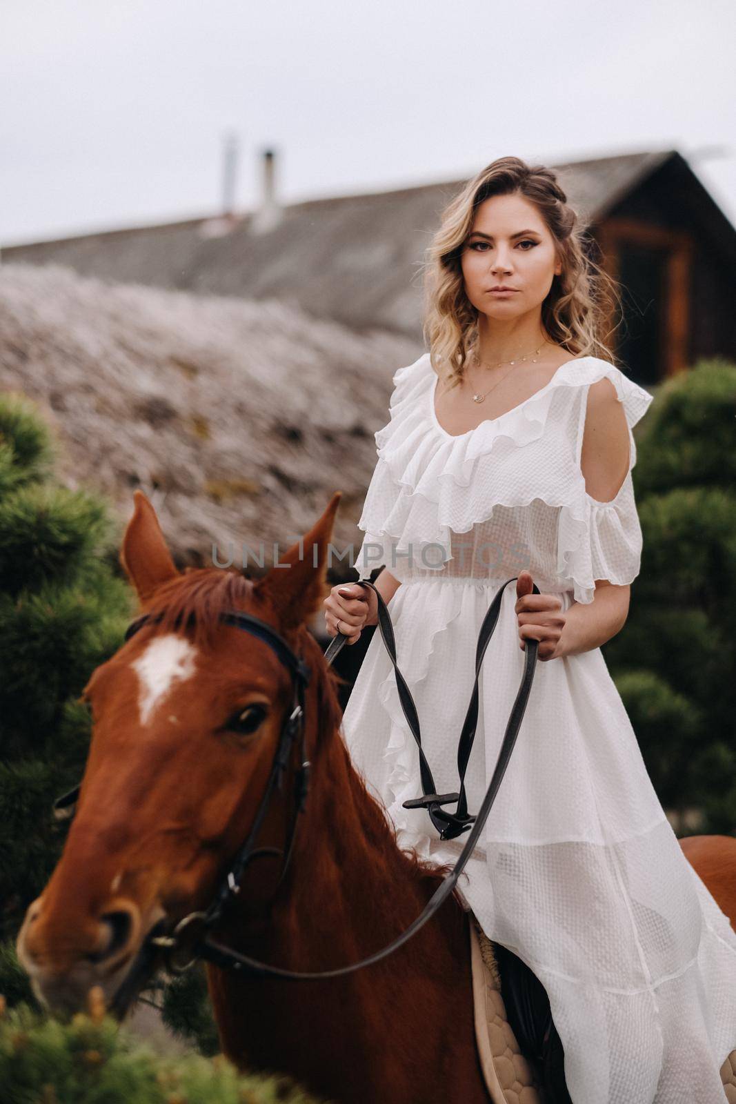 A woman in a white sundress riding a horse near a farm.