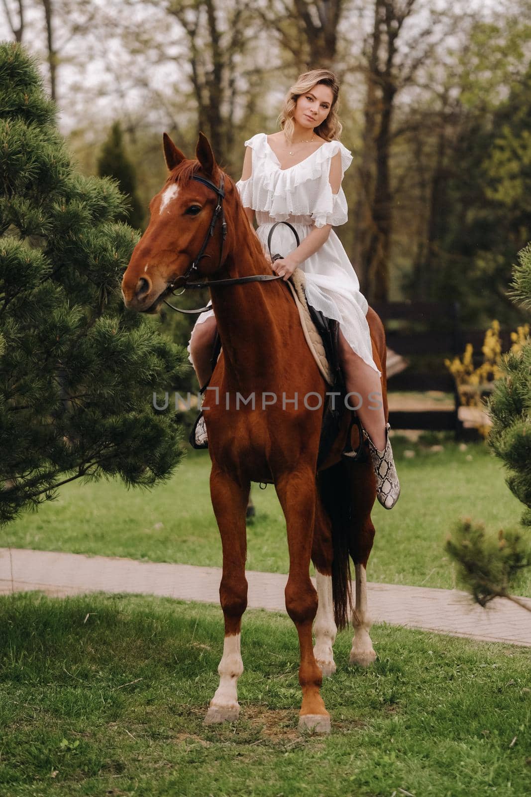 A woman in a white sundress riding a horse near a farm.