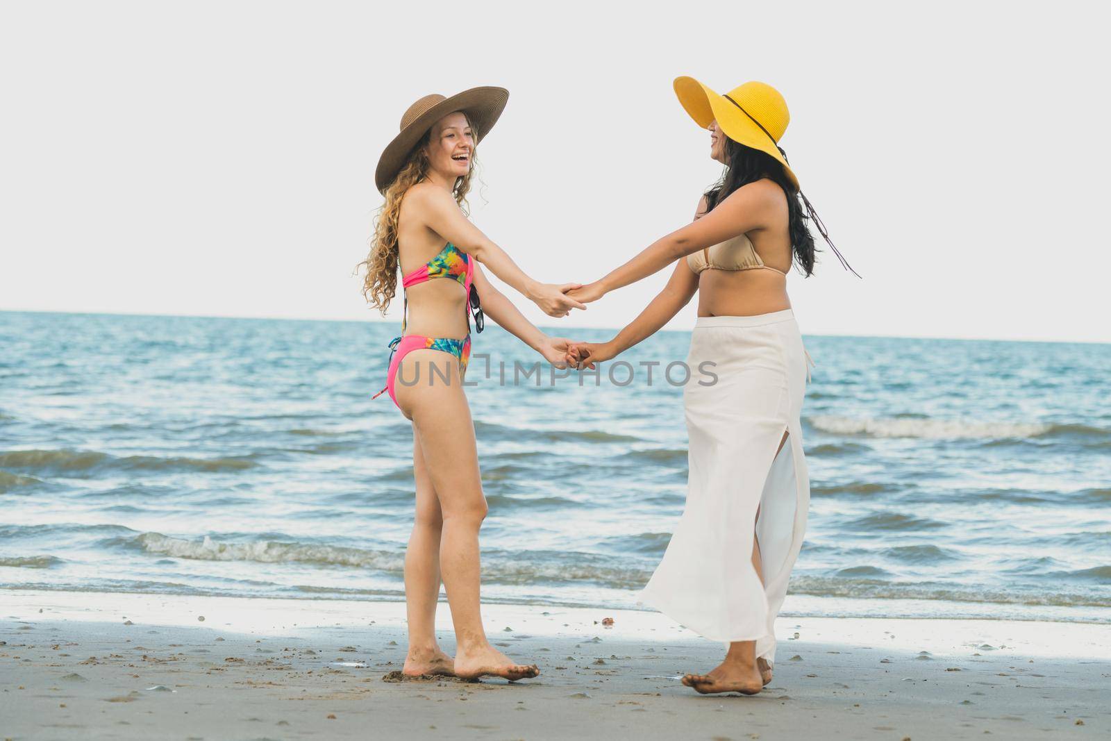 Happy women in bikinis dance together on tropical sand beach in summer vacation. Travel lifestyle.