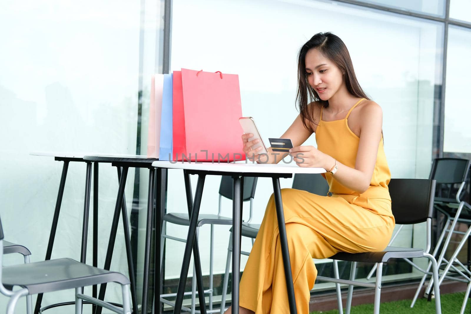 woman holding mobile smart phone & credit card for online payment with colorful shopping bags on table. consumerism lifestyle concept