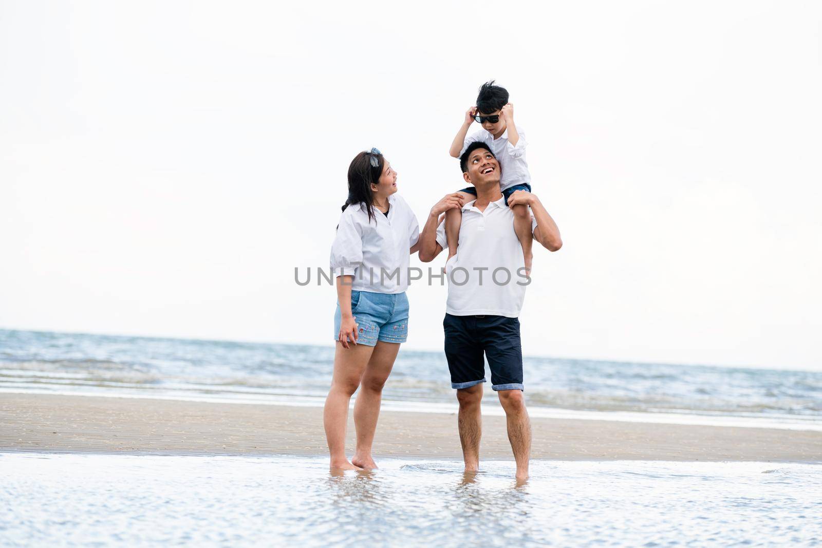 Happy family of father, mother and son goes vacation on a tropical sand beach in summer.