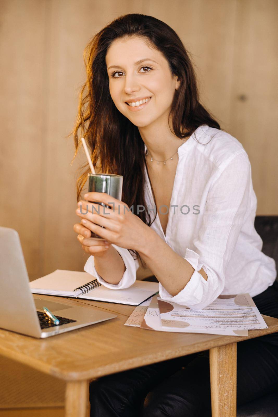 A young freelance woman with a cocktail in her hands at her workplace at work by Lobachad