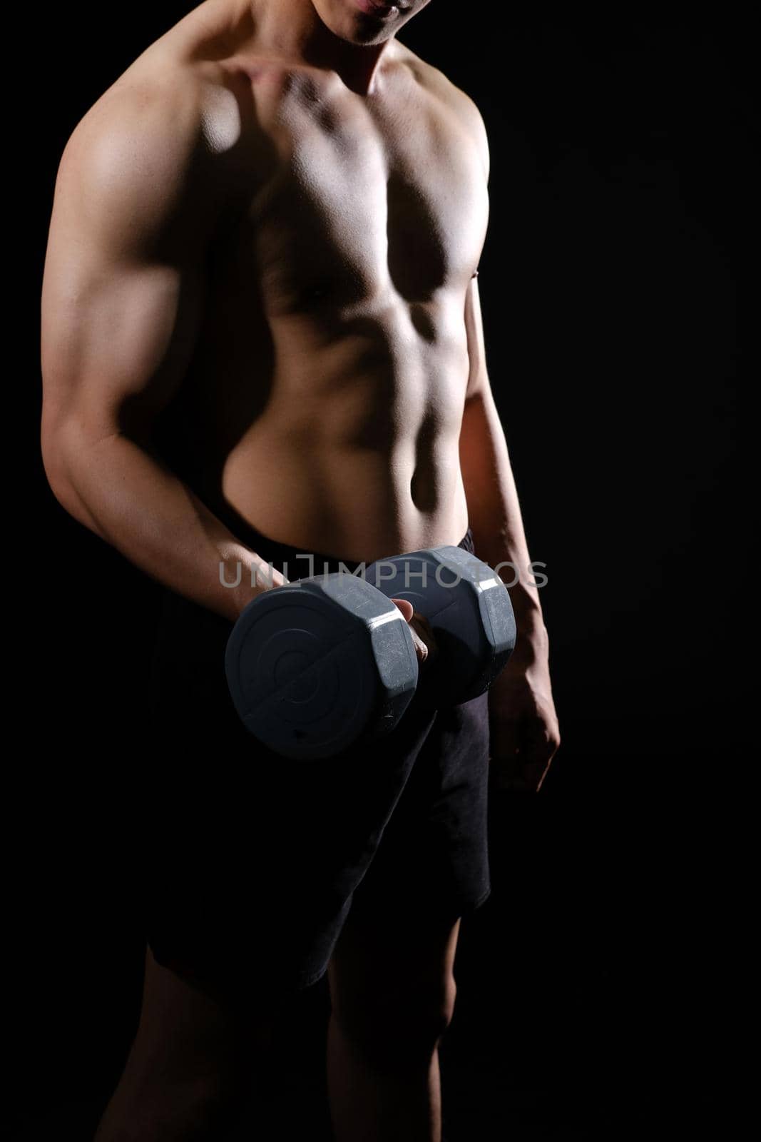 portrait of athletic muscular bodybuilder man with naked torso six pack abs working out with dumbbell. fitness sport exercise concept