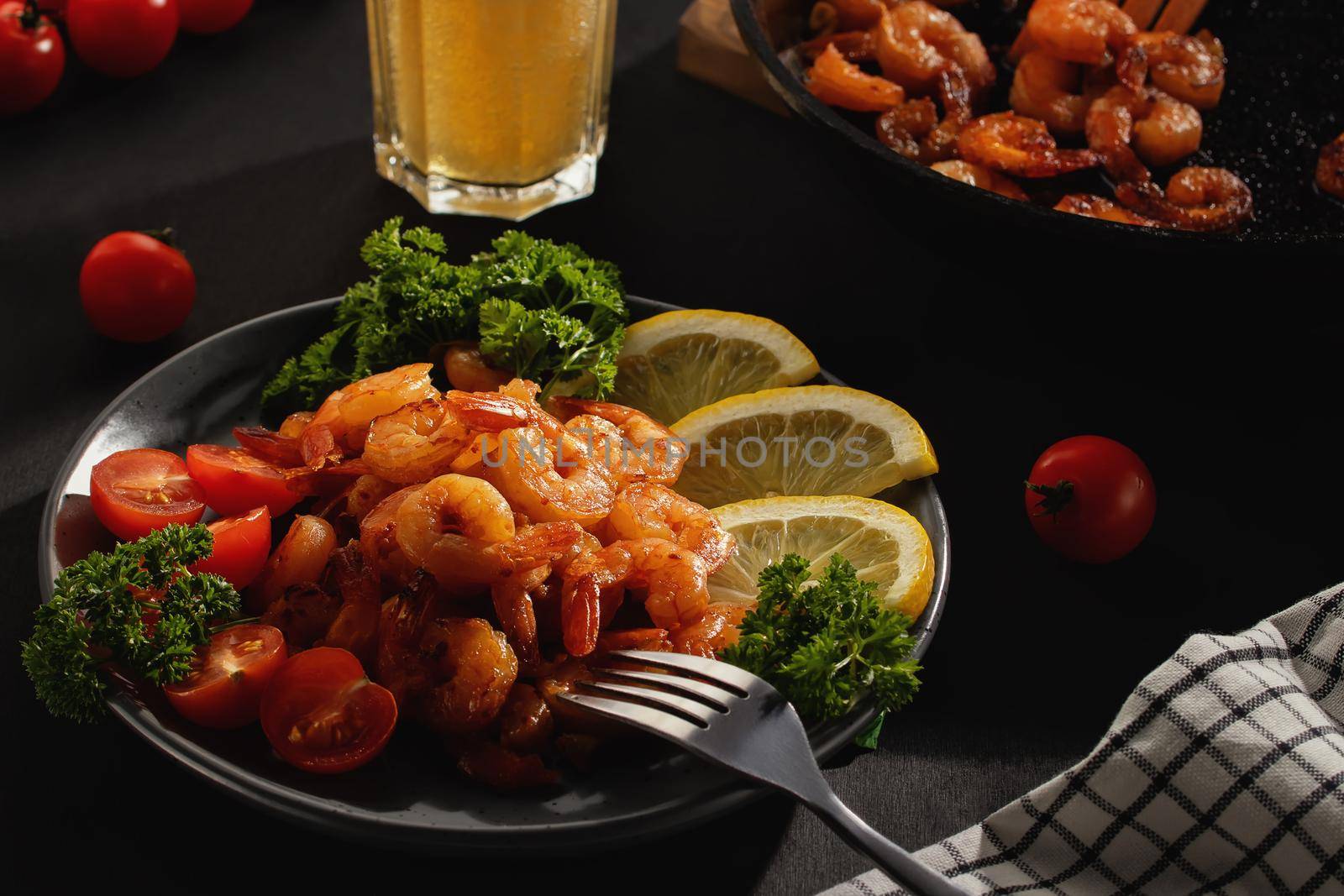 Served dinner - fried shrimp with lemon, tomatoes and herbs and beer in a glass on the table.