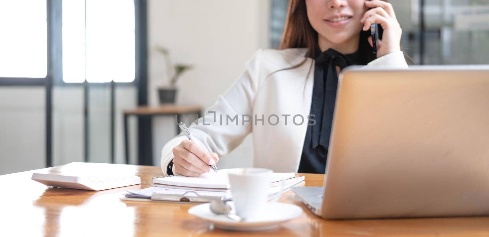 Beautiful young asian woman sitting at coffee shop using smartphone. Happy young businesswoman sitting at table in cafe with tab top computer..