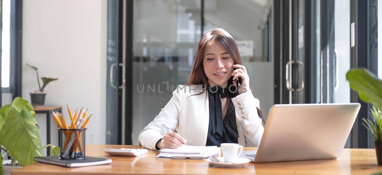 Beautiful young asian woman sitting at coffee shop using smartphone. Happy young businesswoman sitting at table in cafe with tab top computer. by wichayada