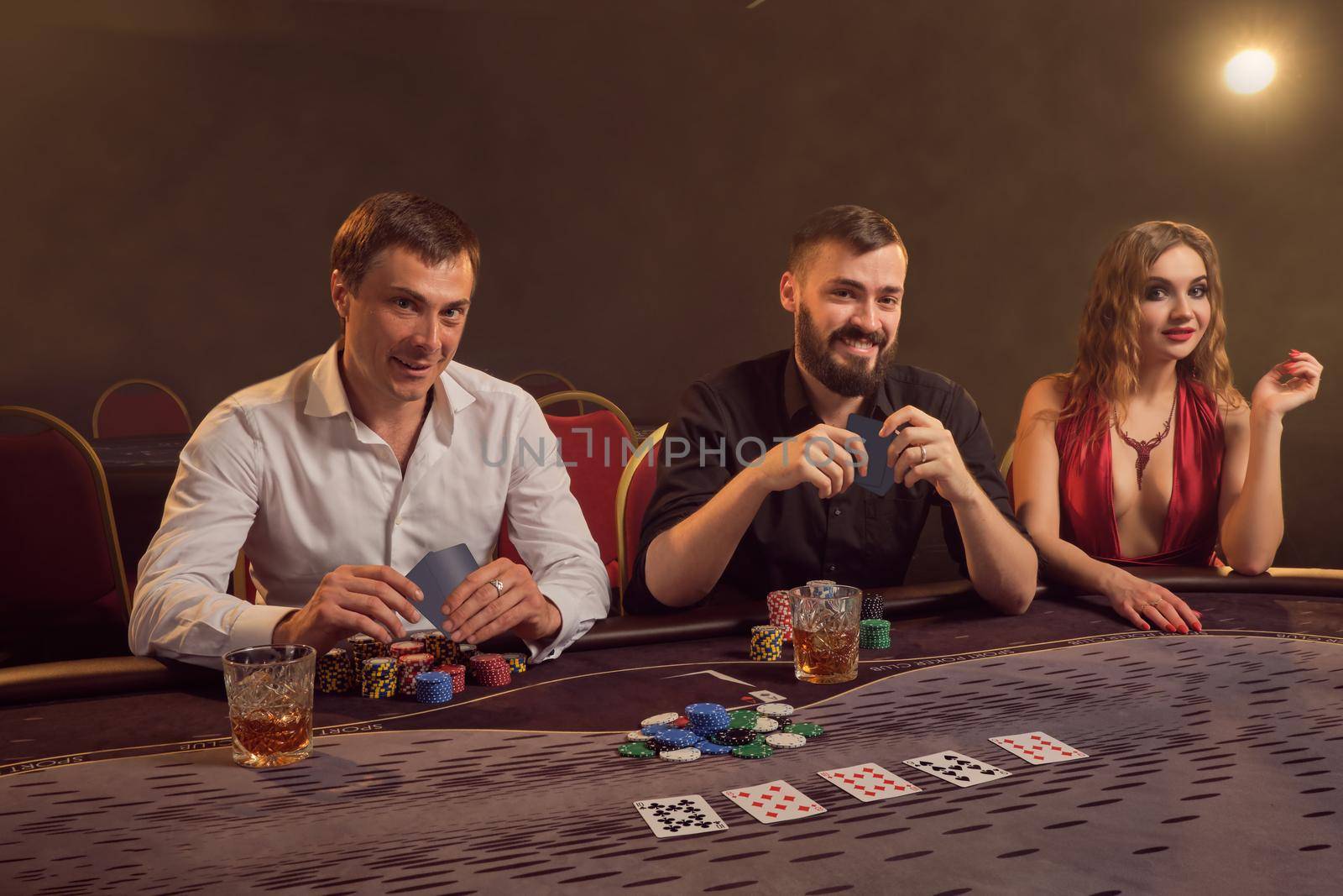 Group of a young wealthy friends are playing poker at a casino. by nazarovsergey