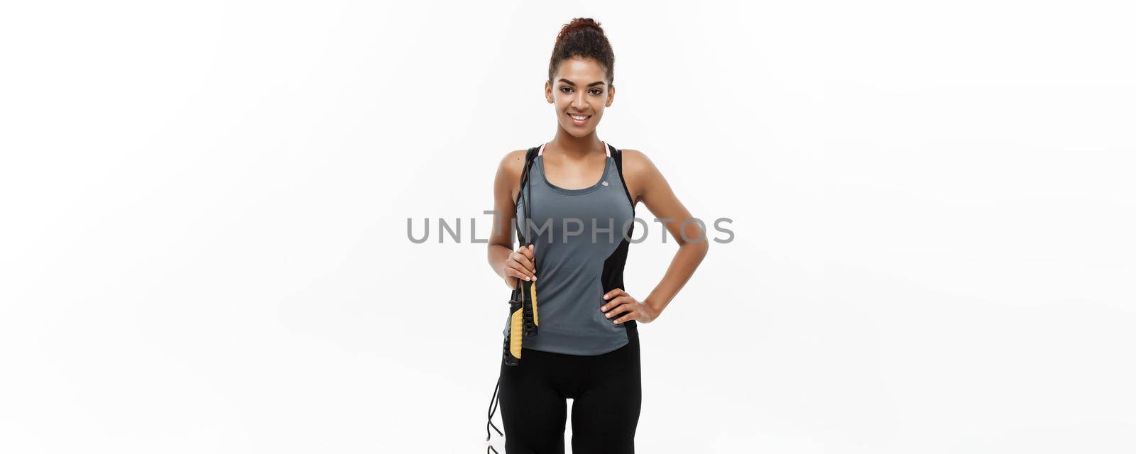 Sport, training, lifestyle and Fitness concept - portrait of beautiful happy African American woman exercising with jumping rope. Isolated on white studio background