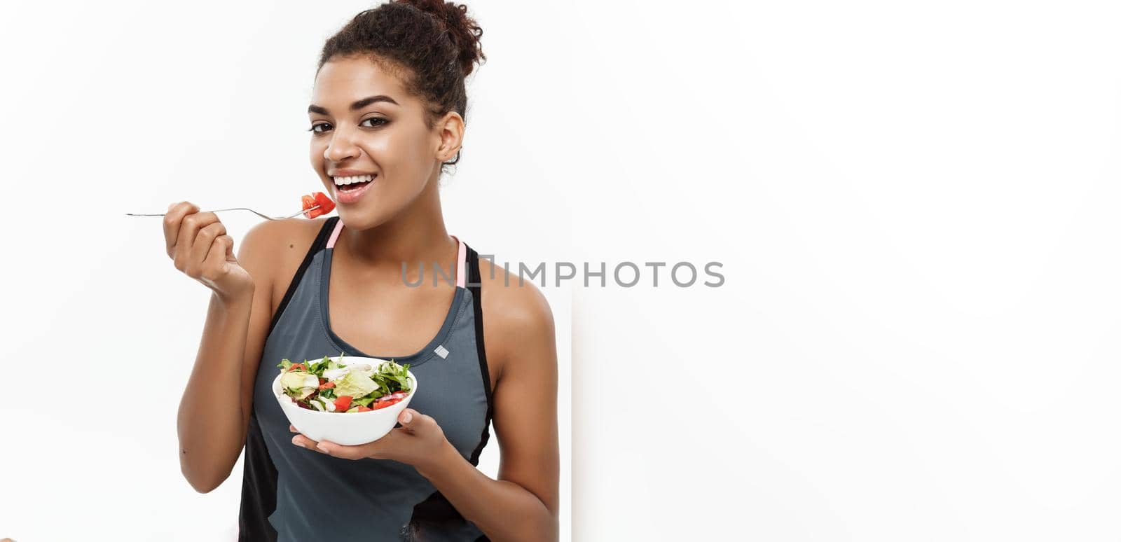 Healthy and Fitness concept - Beautiful American African lady in fitness clothes on diet eating fresh salad. Isolated on white background. by Benzoix