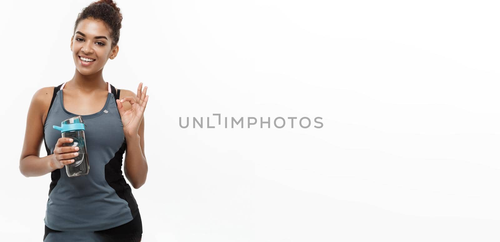 Healthy and Fitness concept - beautiful African American girl in sport clothes holding water bottle after workout. Isolated on white studio background.