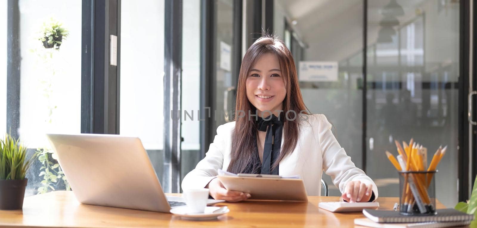 Beautiful smiling Asian businesswoman hand holding pen working using tablet at office. Looking at camera..