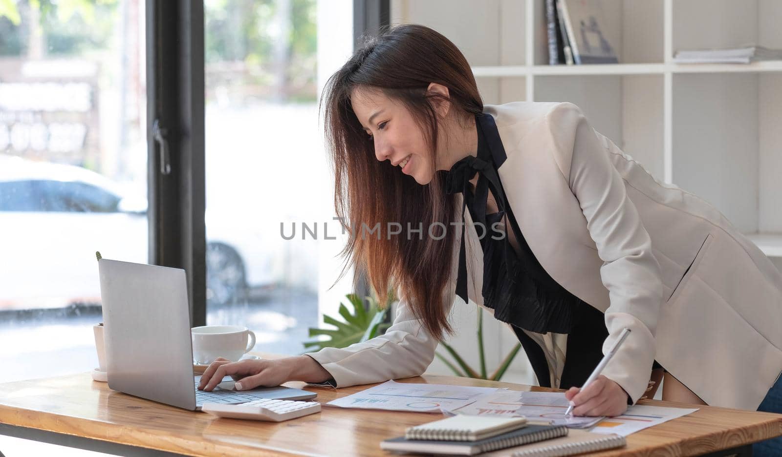 Happy young Asian businesswoman standing using laptop computer at office. by wichayada