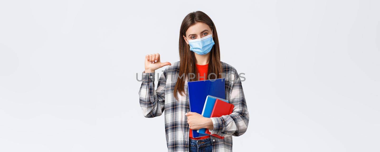 Coronavirus pandemic, covid-19 education, and back to school concept. Confident sassy female student pointing herself, wear medical mask, studying at university, holding notebooks.