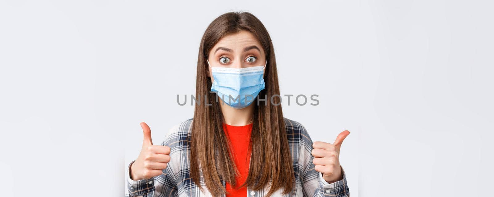 Coronavirus outbreak, leisure on quarantine, social distancing and emotions concept. Sounds good. Excited and pleased, satisfied female in medical mask, show thumb-up, interesting idea.