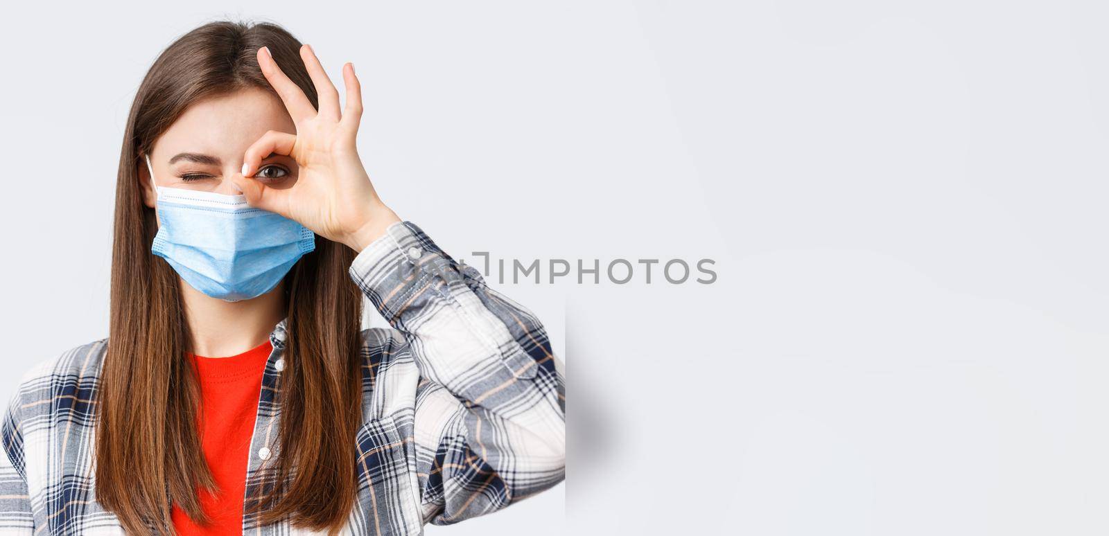 Coronavirus outbreak, leisure on quarantine, social distancing and emotions concept. Close-up of optimistic good-looking woman in medical mask show okay sign and wink.