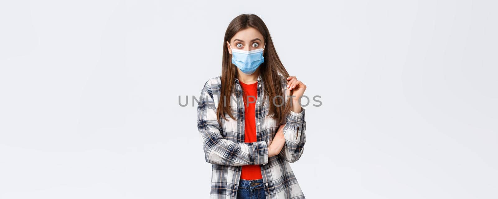 Coronavirus outbreak, leisure on quarantine, social distancing and emotions concept. Shocked and curious young girl in medical mask and checked shirt, stare at friend telling gossip or stunning news by Benzoix