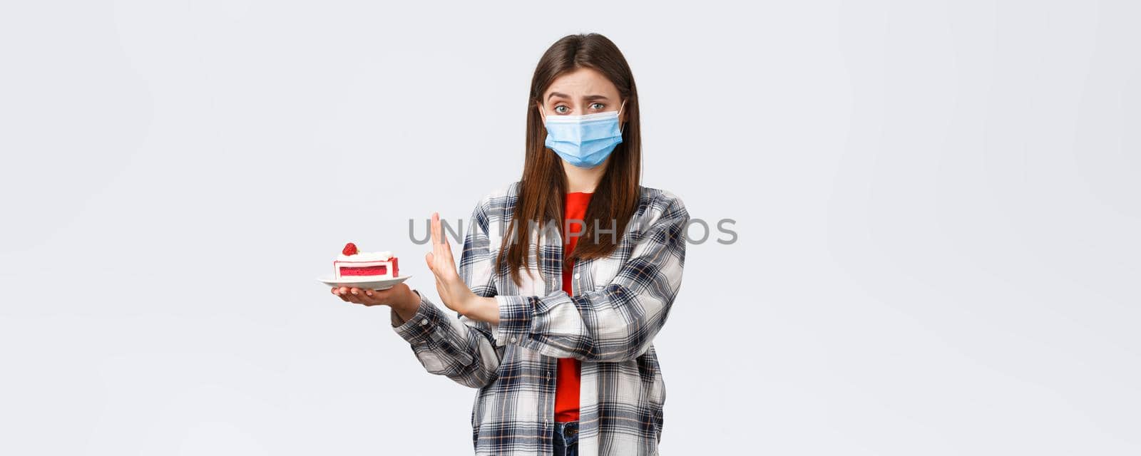 Coronavirus outbreak, lifestyle on social distancing and holidays celebration concept. No thank you. Girl refuse eating this delicious cake as stick to diet, worried over calories, wear medical mask by Benzoix