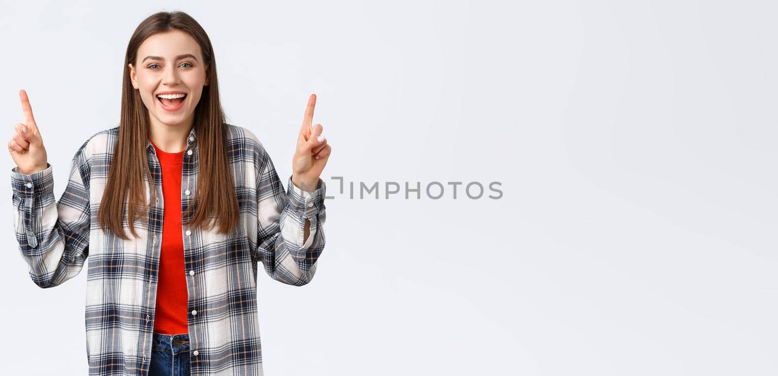 Lifestyle, different emotions, leisure activities concept. Happy beautiful girl in checked shirt, pointing fingers up and laughing carefree, showing good summer vacation ideas, promo or banner.