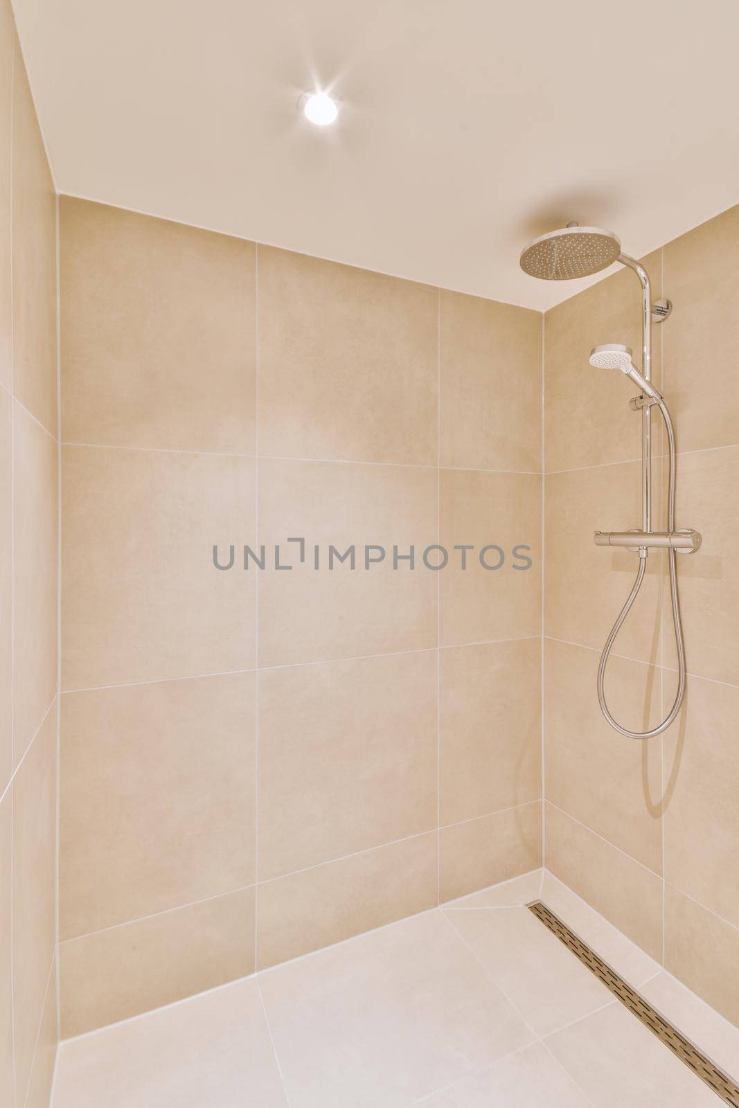 Shower faucets attached to tiled wall near glass partition and ornamental curtail in washroom at home