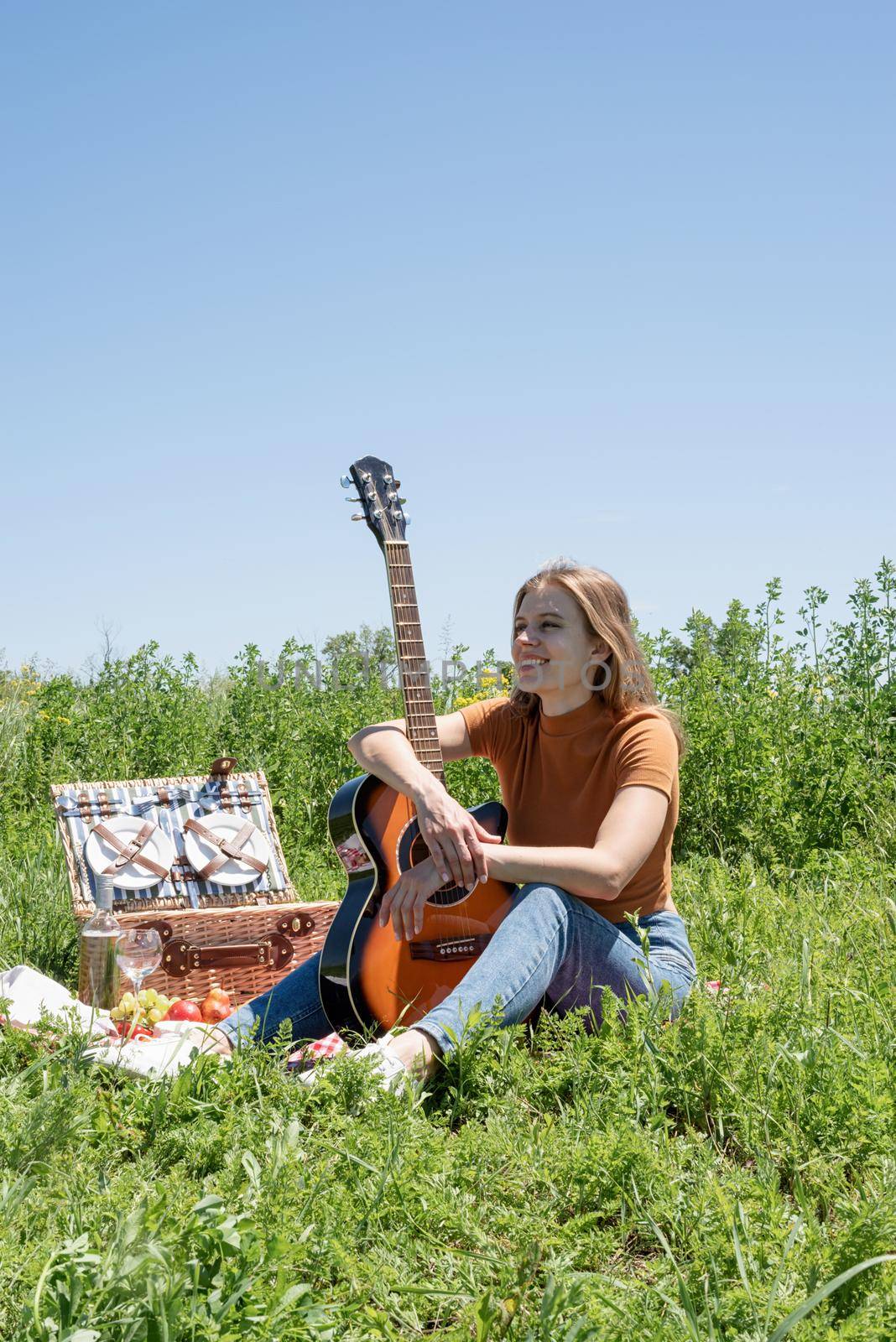 millennial woman in summer clothes and sunglasses playing guitar on a picnic. Happy woman holding her guitar peacefully sitting on grass