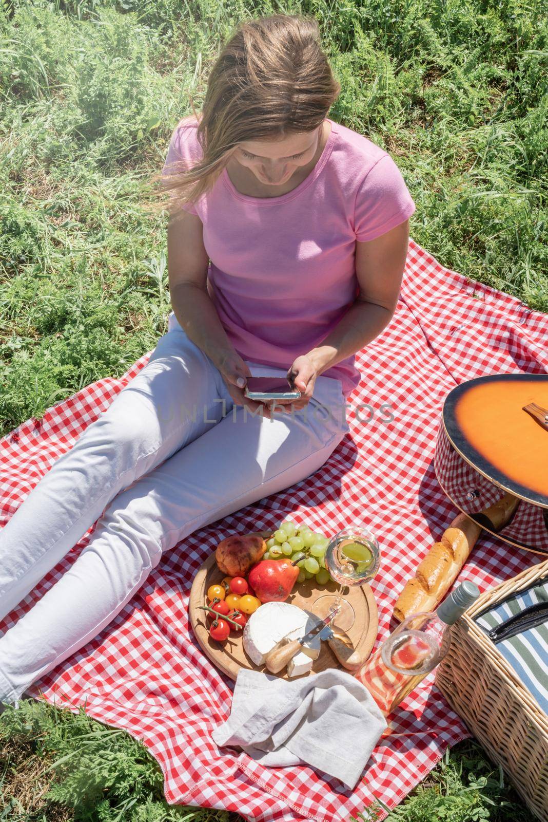 woman in white pants outside having picnic and using smartphone taking photo by Desperada