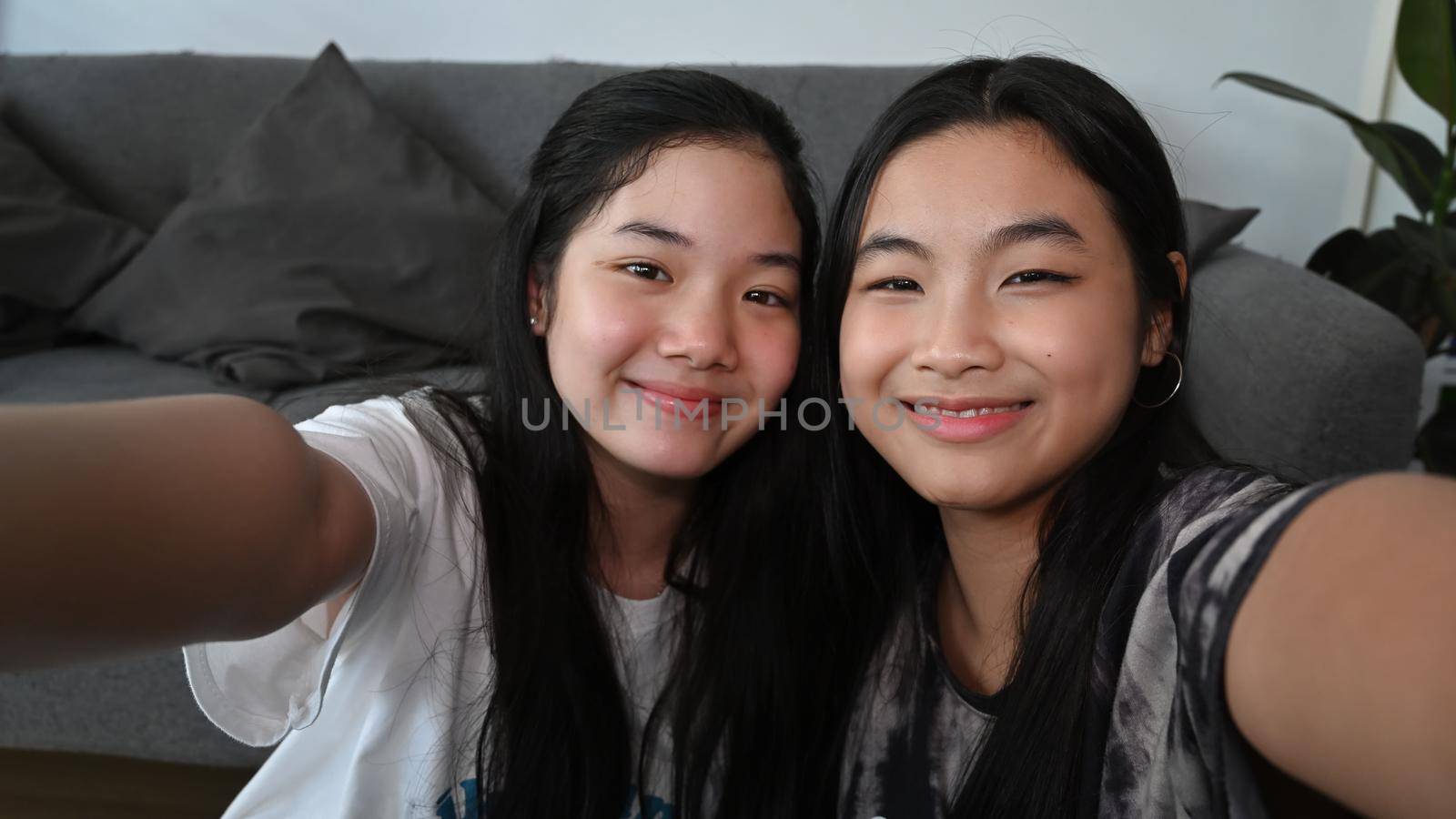 Joyful Asian girls looking at camera make selfie while sitting together in living room. by prathanchorruangsak