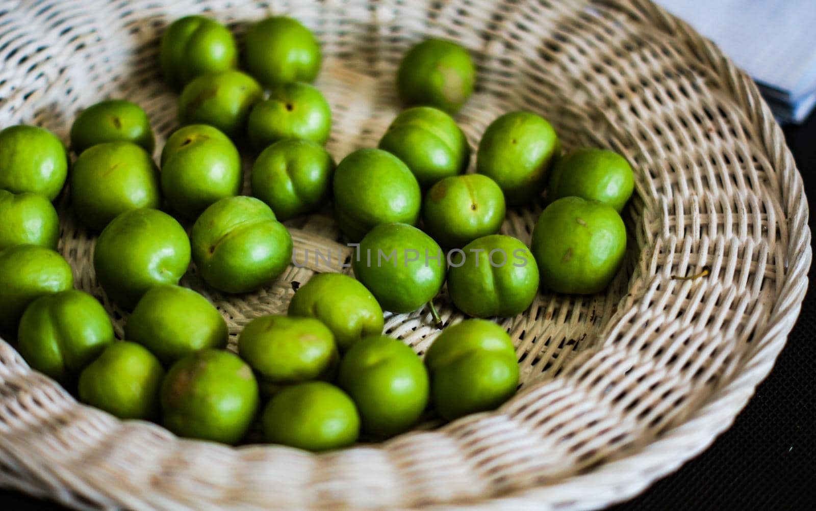 Green cherry plum in white straw plate by Elet