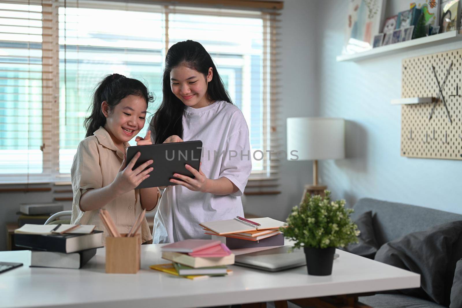 Two asian girl doing online homework or surfing internet with digital tablet at home.