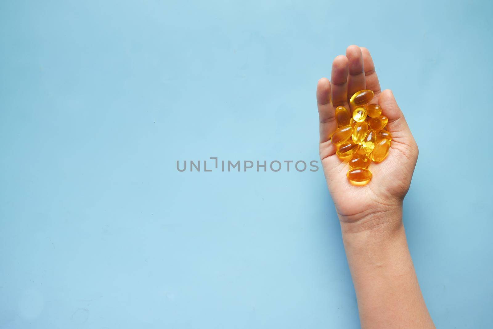 fish oil supplement on hand on blue background .